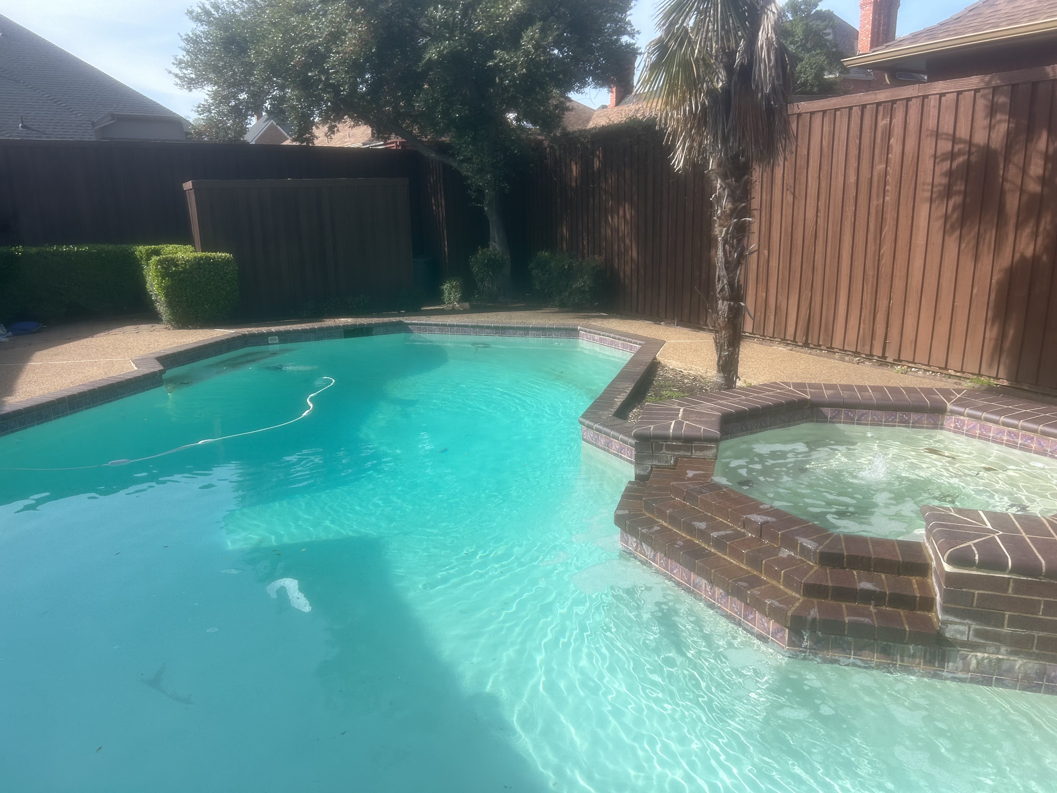 The same brick-edged pool before service — duller water, vacuum hose crossing the pool