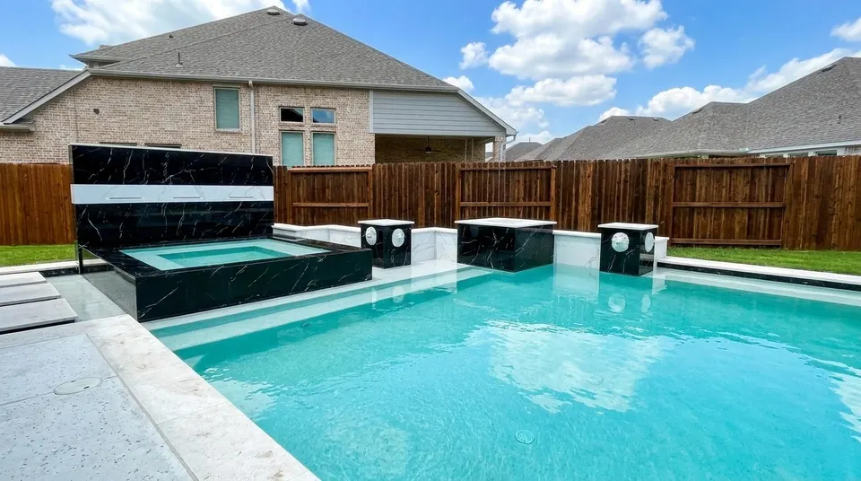 Black-marble raised spa and media wall with white marble pedestals on a modern gunite pool